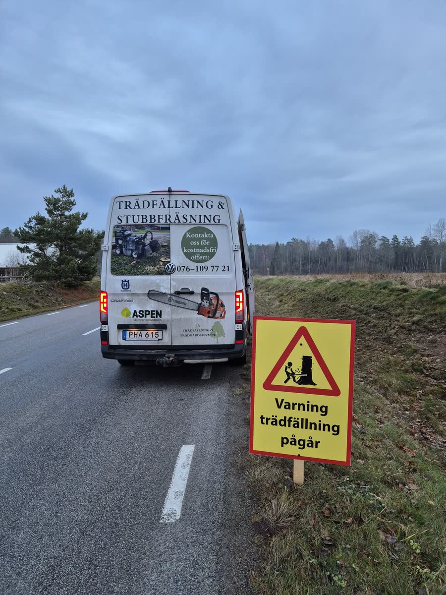 Varningsskylt med texten Varning trädfällning pågår vid företagets servicebuss på en landsväg.
